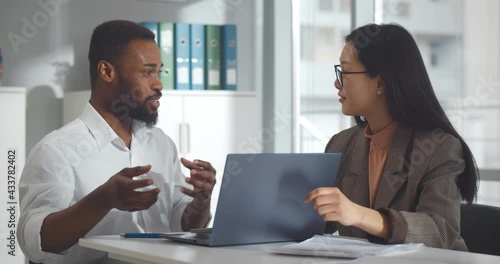Diverse business colleagues looking at laptop and discussing project in office