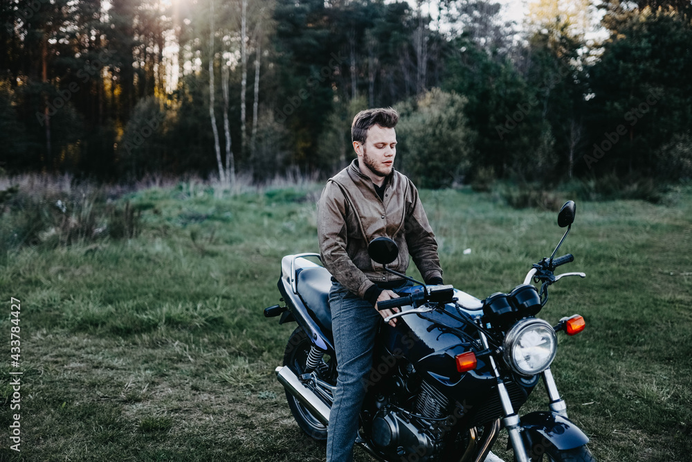 man in a leather brown jacket and a motorcycle in the summer forest, a city motorcycle. motorcyclist biker man in a leather brown jacket and a motorcycle in the summer forest, a city motorcycle. motorcyclist biker