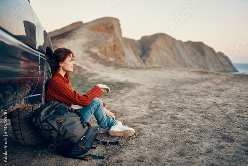 a traveler sits near a car in the mountains in nature and admires the landscape at sunset