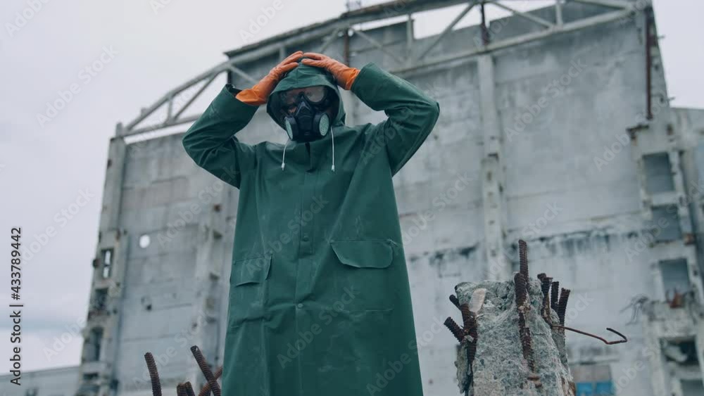 Survivor in infected zone. Man in protective suit and gas mask putting hood to protect himself from chemical attack in abandoned place. Survivor in infected zone. Man in protective suit and gas mask putting hood to protect himself from chemical attack in abandoned place.