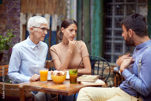 Two female friends of different generations accusing their young male friend for something while they have a drink in the bar. Leisure, bar, friendship, outdoor