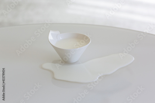 a cup of milk on a white table spilled milk