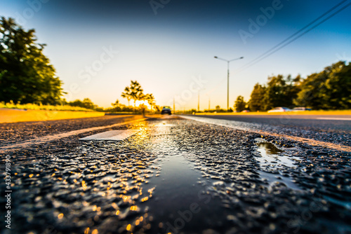 Sunset after rain, the parked car on the highway. Wide angle view close up with puddles on the asphalt level