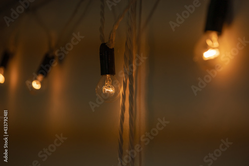Round small bulbs glowing with warm light hang on a white wall. Loft-style decor. The bulbs are connected to each other by a spiral cord like a garland