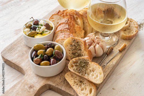 Snack board with wine glasses, fresh bread, pickled olives and mozzarella cheese on wooden tray over white background.