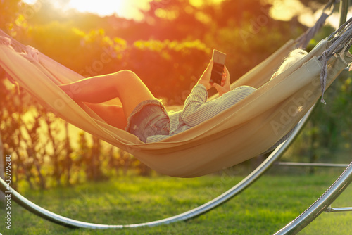 Woman relaxing at sunset on a hammock with her mobile