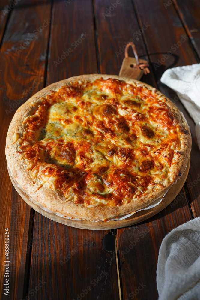A big round pizza with cheese and tomato sauce on a dark wooden table A big round pizza with cheese and tomato sauce on a dark wooden table