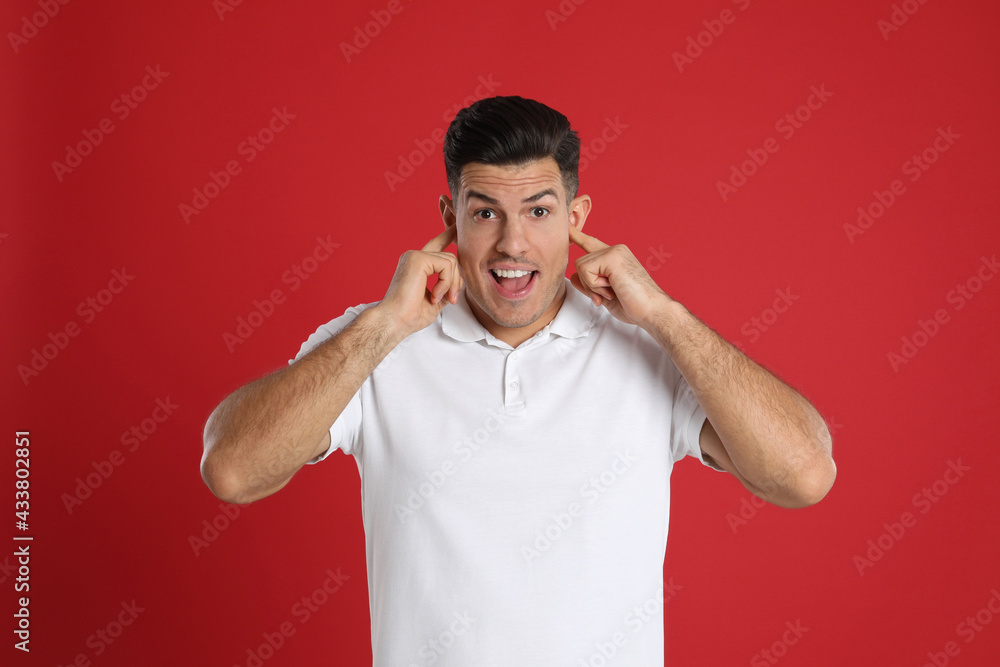 Excited man covering ears with fingers on red background Excited man covering ears with fingers on red background