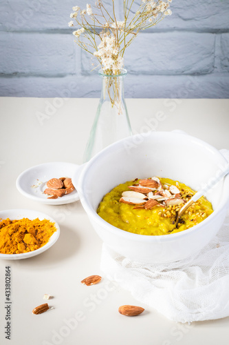 Golden oatmeal porridge in bowl with turmeric, and almonds, healthy breakfast food.