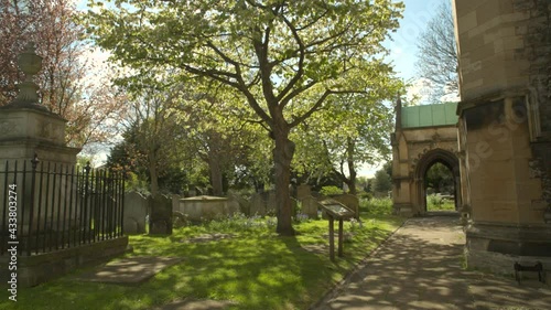 English churchyard with graves, a tomb, a cherry tree and the side of a gothic church. Sunlight through the branches.