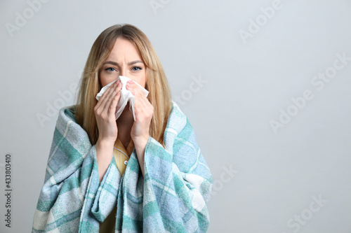 Fotografiet Young woman with blanket suffering from runny nose on light background