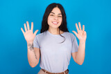 young beautiful tattooed girl wearing blue t-shirt standing against blue background showing and pointing up with fingers number nine while smiling confident and happy.