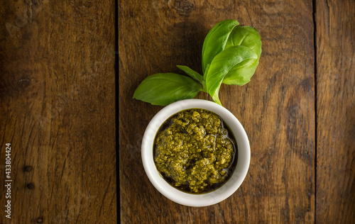 Green pesto sauce in a white bowl with fresh Basil on rustic wooden table