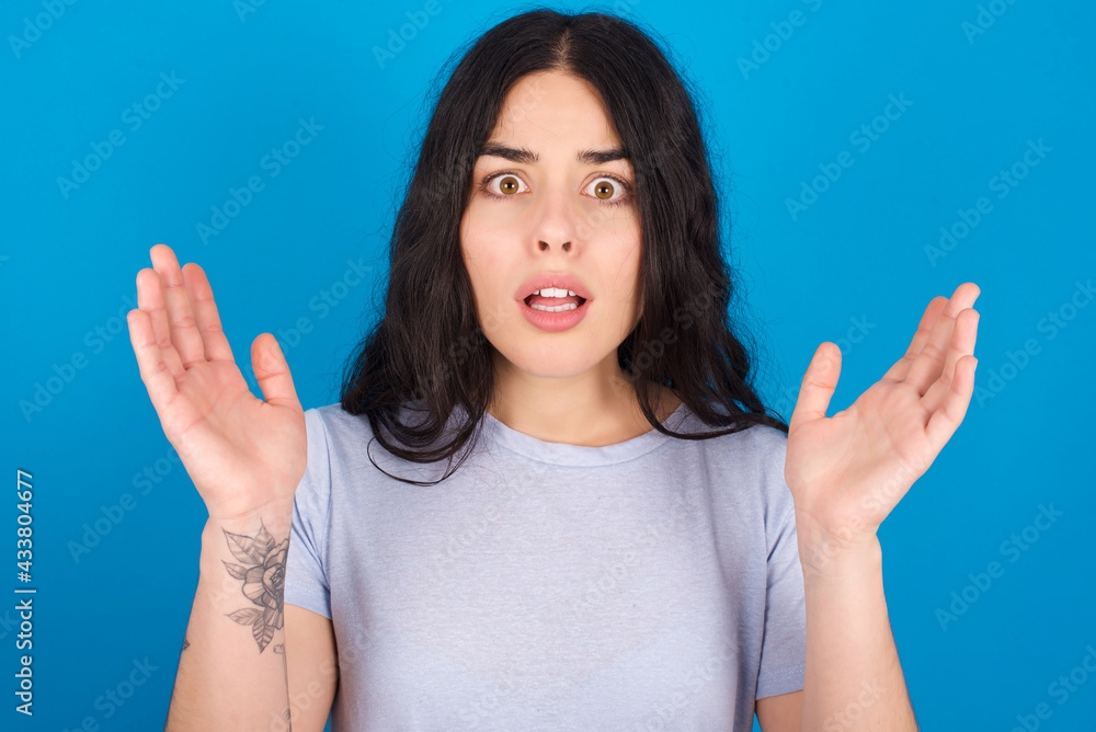 Surprised terrified young beautiful tattooed girl Gestures with uncertainty, stares at camera, puzzled as doesn't know answer on tricky question, People, body language, emotions concept Surprised terrified young beautiful tattooed girl Gestures with uncertainty, stares at camera, puzzled as doesn't know answer on tricky question, People, body language, emotions concept