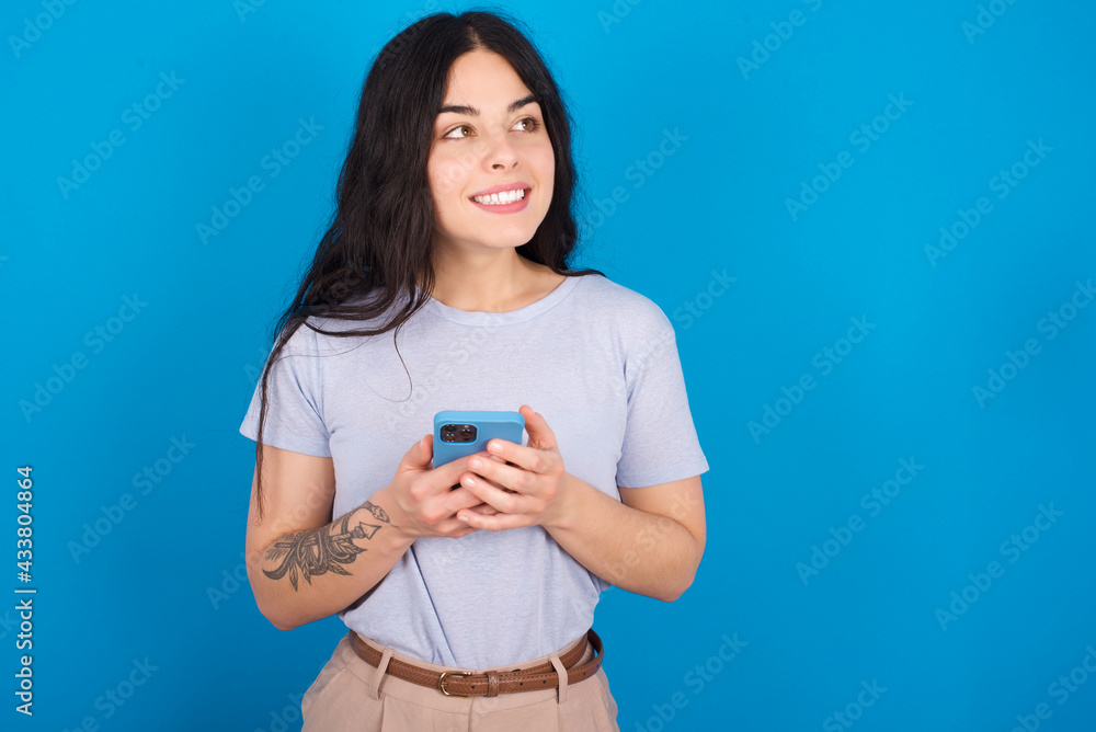 young beautiful tattooed girl wearing blue t-shirt standing against blue background holding in hands showing new cell young beautiful tattooed girl wearing blue t-shirt standing against blue background holding in hands showing new cell