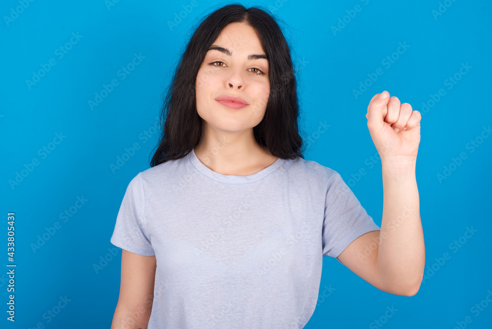 young beautiful tattooed girl wearing blue t-shirt standing against blue background pointing up with fingers number ten in Chinese sign language Shi young beautiful tattooed girl wearing blue t-shirt standing against blue background pointing up with fingers number ten in Chinese sign language Shi