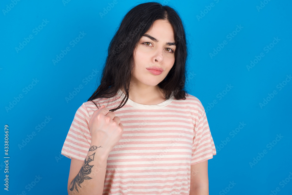 young beautiful tattooed girl wearing pink striped t-shirt standing against shows fist has annoyed face expression going to revenge or threaten someone makes serious look. I will show you who is boss young beautiful tattooed girl wearing pink striped t-shirt standing against shows fist has annoyed face expression going to revenge or threaten someone makes serious look. I will show you who is boss