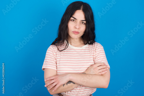 young beautiful tattooed girl wearing pink striped t-shirt standing against blue background Pointing down with fingers showing advertisement, surprised face and open mouth