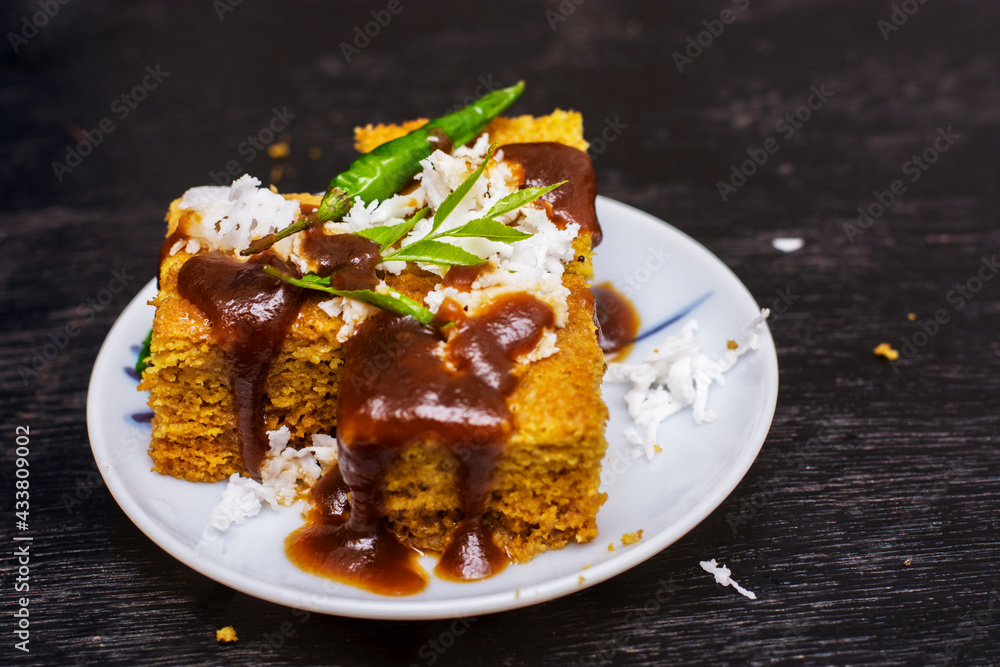 Gujarati khaman Dhokla made with chana dal served with coconut and chutni on a white plate and black background. Gujarati khaman Dhokla made with chana dal served with coconut and chutni on a white plate and black background.