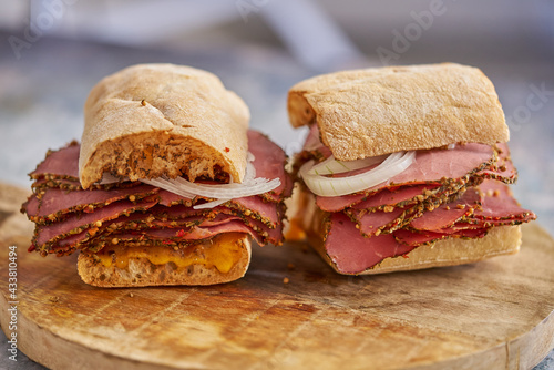 Thin cut pastrami sandwhich with delicious meet on baguette bread with chedder cheese, onion photo