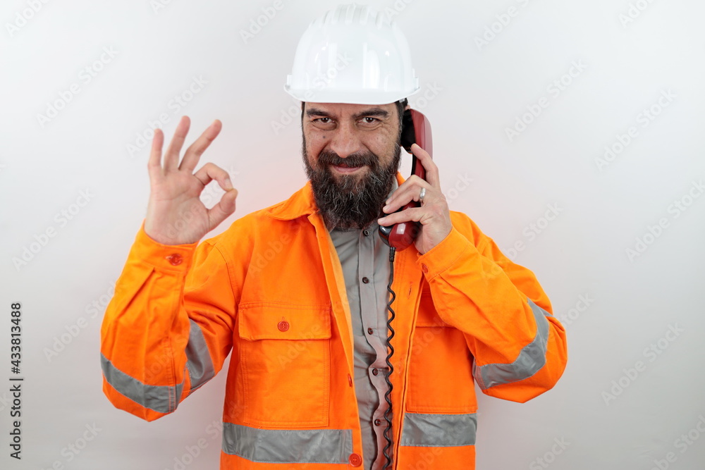 Architect wearing hardhat, standing smiling happy speaking on phone making ok hand sign looking at the camera. Architect wearing hardhat, standing smiling happy speaking on phone making ok hand sign looking at the camera.