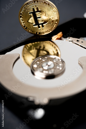 Gold Bitcoin reflecting on hard drive platter of hard disk storage. Digital crypto currency and blockchain technology concept
