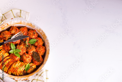 Homemade meatballs with tomato sauce in a white dish baked in the oven with herbs on marble white background