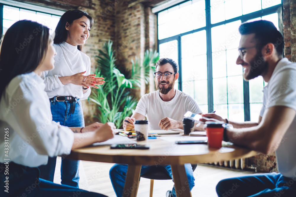 Positive young diverse managers sitting at table with takeaway coffees during meeting in workspace Positive young diverse managers sitting at table with takeaway coffees during meeting in workspace