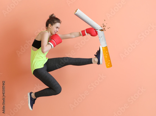 Jumping sporty woman in boxing gloves kicking cigarette on color background photo