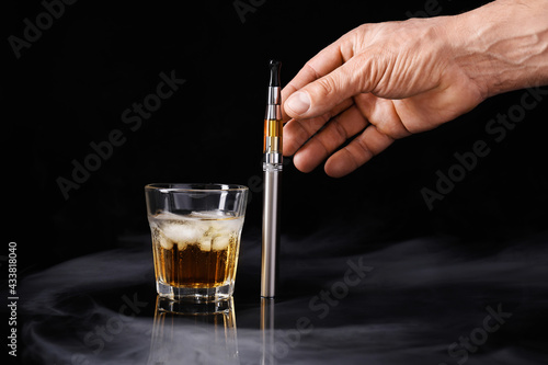 Male hand with electronic cigarette and glass of whisky on dark background