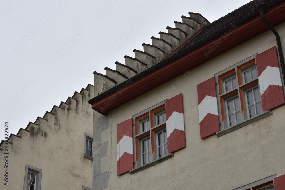 Castle in city Tiengen, Germany. Detail of facade with two windows and shutters in red and white colors and articulated roof edges. Photo made in low angle view. There is overcast sky on background. 