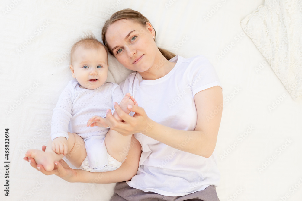 portrait of a mother with a baby in her arms gently embracing him on a white bed at home, mother's love portrait of a mother with a baby in her arms gently embracing him on a white bed at home, mother's love
