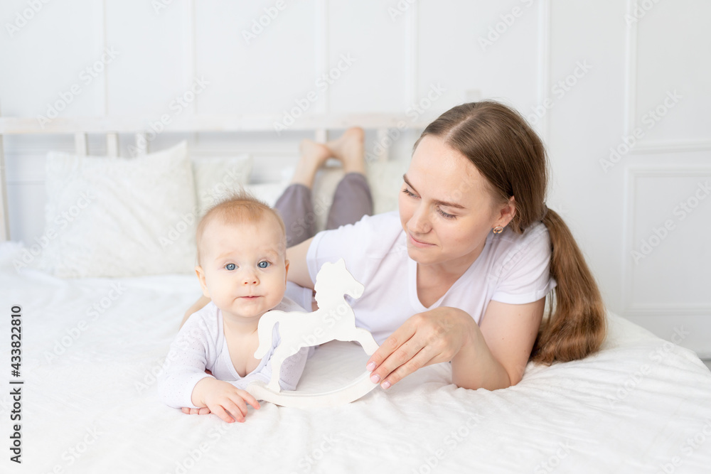 mom plays with baby wooden toy horse on the bed at home, happy family mom plays with baby wooden toy horse on the bed at home, happy family