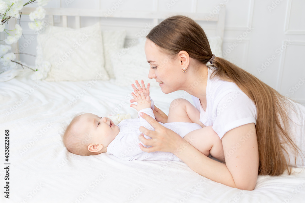 happy mother with baby playing and cuddling gently on the bed at home happy mother with baby playing and cuddling gently on the bed at home