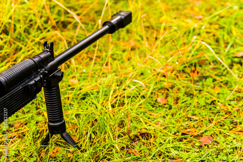 Rifle standing on a bipod on a ground in the grass after a rain. Close up view of a grass level