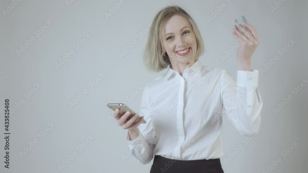 Young happy beautiful woman holding smartphone and bank card rejoices in winning lottery. 4K video. Young happy beautiful woman holding smartphone and bank card rejoices in winning lottery. 4K video.