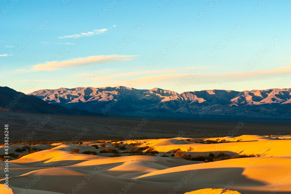 Desert landscape with dunes and mountains at sunrise.