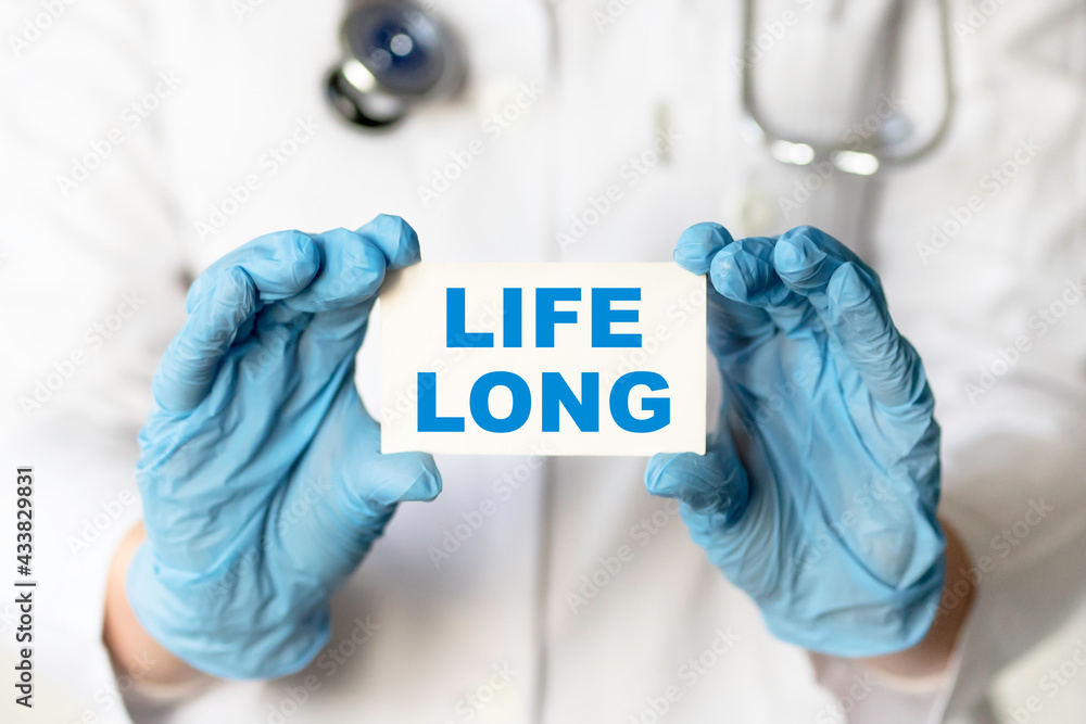 A medical worker in gloves holds a card with the words LIFE LONG. Medical concept. A medical worker in gloves holds a card with the words LIFE LONG. Medical concept.