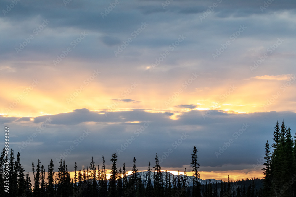 Fototapeta premium Stunning sunset rays shining bright along the Alaska Highway during springtime in northern Canada.
