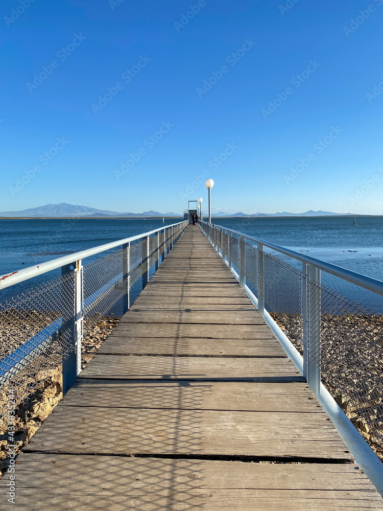 Wooden fishing pier view in San Rafael, Mendoza. Close up of the dock and background of the lake and the mountains on a clear summer day.