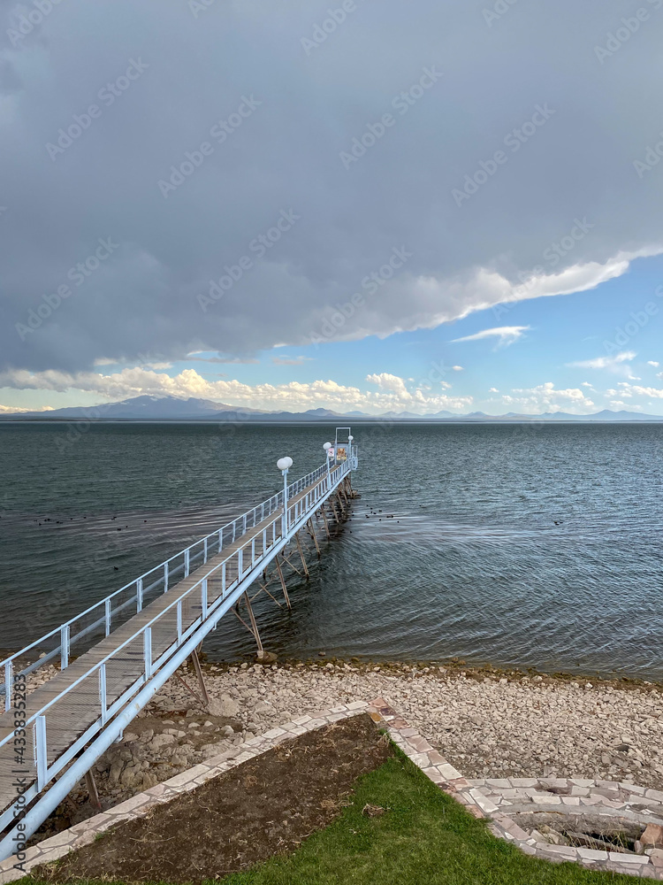 Fishing pier on lake on a cloudy day. Calm waters with a background of the mountains in San Rafael, Mendoza. Dense gray clouds covering the sky.