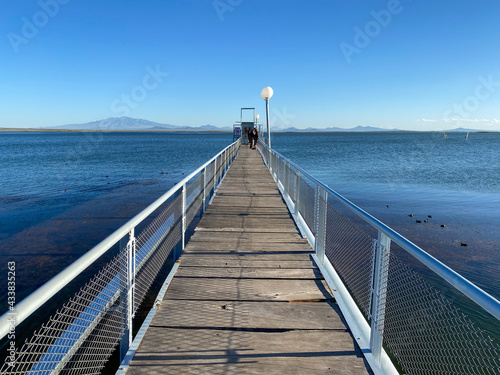 Close view of the wooden fishing pier over the blue lake in San Rafael, Mendoza, Argentina. Calm extensive waters below a blue clear sky.