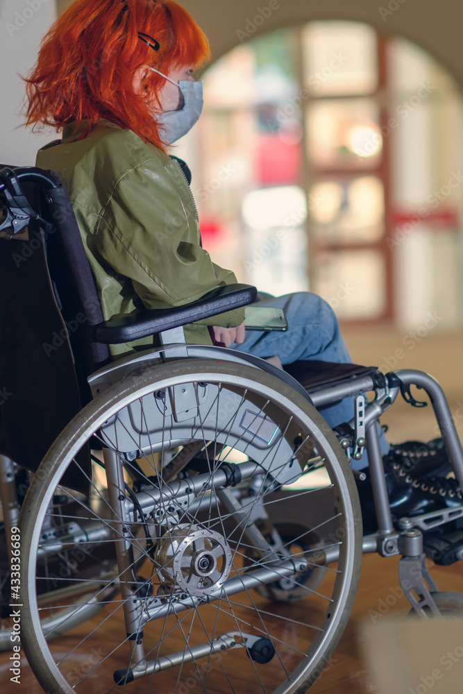 Obraz premium Disabled girl with red hair wearing a mask in a wheelchair, selective focus
