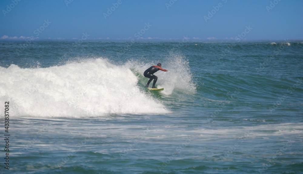 Surfista masculino com uma prancha amarela a surfar na crista de uma onda, com fato de neoprene vestido Surfista masculino com uma prancha amarela a surfar na crista de uma onda, com fato de neoprene vestido