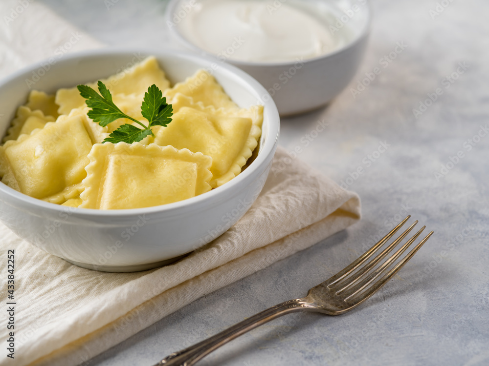 Ravioli. Nice presentation. Decorated with a sprig of mint. White background. White earthenware dishes. Next - sour cream sauce, fork. White tablecloth and white napkin. Ravioli. Nice presentation. Decorated with a sprig of mint. White background. White earthenware dishes. Next - sour cream sauce, fork. White tablecloth and white napkin.