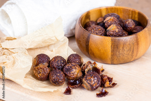 Brown dry soap nuts (Soapberries, Sapindus Mukorossi) in a wooden bowl for organic laundry and gentle natural skin care on light background.