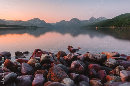 Close up of the giant colorful pebbles of Lake McDonald with the towering Rocky Mountain peaks, lake reflections and a colorful pink, orange sunset at Glacier National Park, Montana, USA. photo
