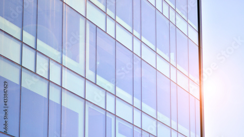 Modern glass building and rising sun. Glass facade on a bright sunny day with sunbeams in the blue sky. Economy, finances, business activity concept. 