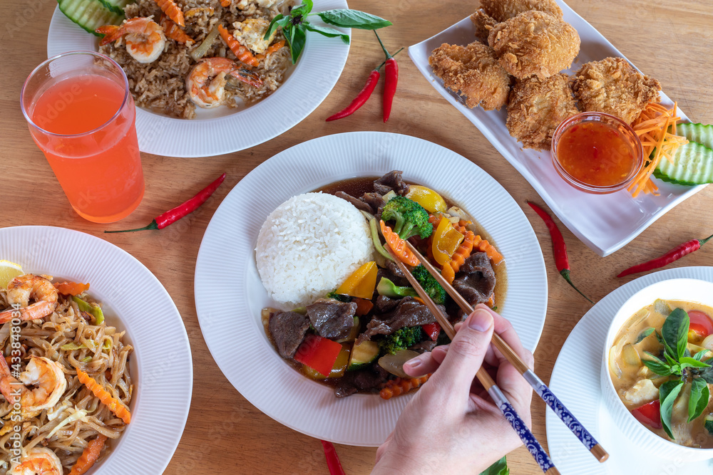 A top-down view of several varieties of Thai food with pares chopsticks in hand with wood background. Bamboo shoots, Glass noodles, Carrot, Oyster sauce, Rice, shrimp, Cabbage, onions, strong basil, A top-down view of several varieties of Thai food with pares chopsticks in hand with wood background. Bamboo shoots, Glass noodles, Carrot, Oyster sauce, Rice, shrimp, Cabbage, onions, strong basil,