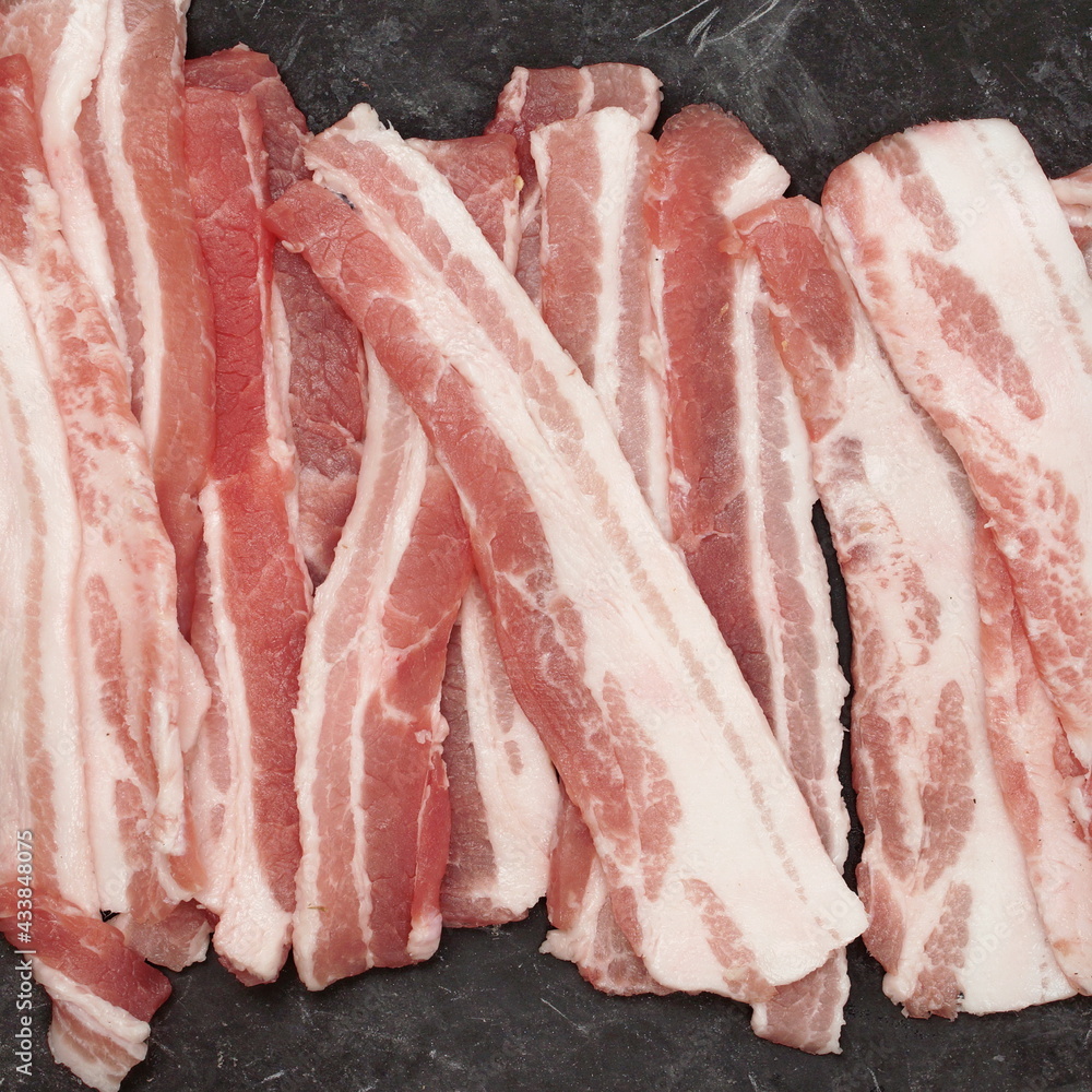 Cold Sliced Bacon On Black Table Grunge Background, Overhead View. Streaky Fresh Bacon Top View. Cold Sliced Bacon On Black Table Grunge Background, Overhead View. Streaky Fresh Bacon Top View.